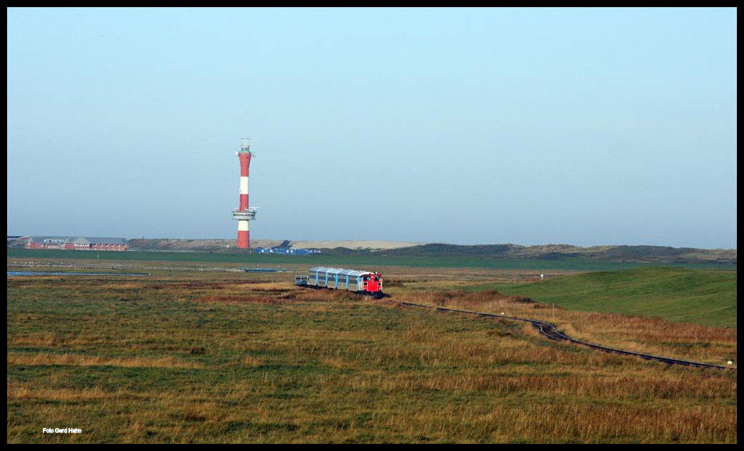 Die Bahnstrecke vom Hafen zum Ort Wangerooge führt in einem weiten Bogen durch das Watt, bevor die Strecke durch ein Deichtor gesichertes Terrain erreicht. Hier ist am 1.10.2017 Schöma Lok 399108 mit einem Personenzug außerhalb der Deichanlagen in Richtung Bahnhof unterwegs. Im Hintergrund ist der neue Leuchtturm von Wangerooge zu sehen.