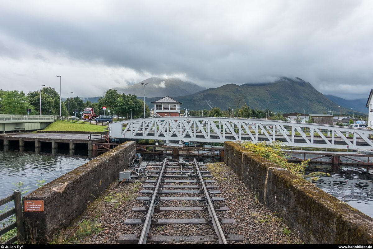 Die Banavie Railway Swing Bridge über den Caledonian Canal während dem Schliessvorgang am 25. August 2017. Aufgenommen von einem unbewachten Bahnübergang (ein Zug konnte logischerweise nicht kommen). Im Hintergrund das Kontrollzentrum, von wo aus die gesamte West Highland Line zwischen Helensburgh, Oban und Mallaig überwacht wird, die mit Radio Electronic Block gesichert ist.