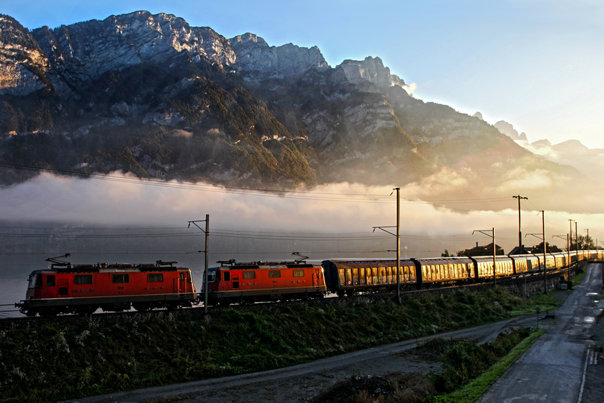 Die beiden Re 4/4 II Loks 11313 und 11293 im Streiflicht,kommen wenige Sekunden nach Sonnenaufgang mit einem im Morgenlicht golden aufglänzenden Ganzzug aus Schiebewandwagen bestehend,bei Mühlehorn vorbeigedonnert.Bild vom 7.10.2014