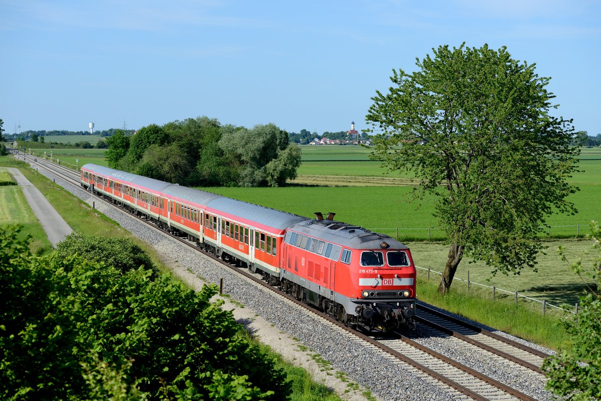 Die bestens gepflegte Kemptener 218 472 passiert mit ihrem RE 57592 die leider immer mehr zuwachsende Fotostelle bei Weinhausen. Im Hintergrund erkennt man die Kirche von Jengen und den markanten Wasserturm in Buchloe (06. Juni 2014).