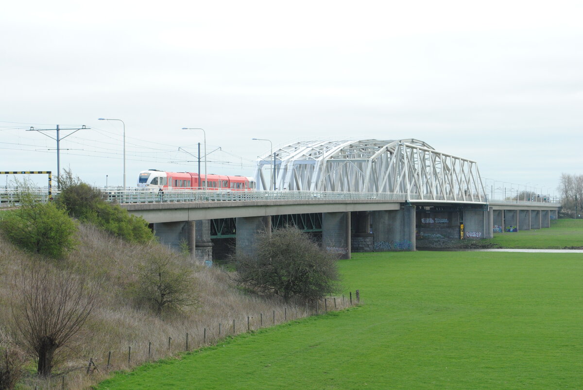 Die Brücke über den IJssel zwischen Westervoort und Arnhem. Von links nach rechts: Eisenbahnbrücke (2 Gleise), Strassenbrücke und Fahrradbrücke. Arriva 375 als Zug 30930 von Winterswijk nach Arnhem Centraal kommt vorbei. Arnhem, 02.04.2023. Bild 22898.