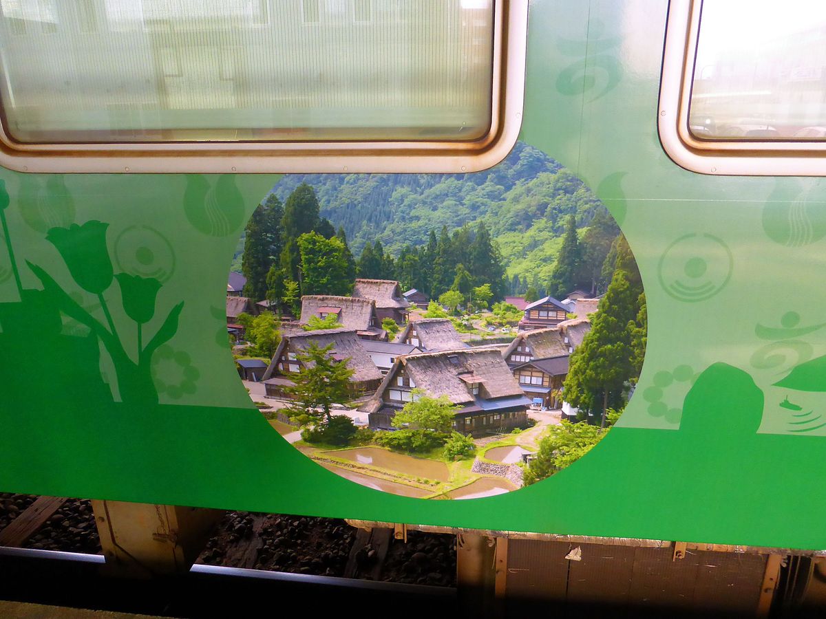 Die bunten Triebwagen der Region Takaoka: Auf der einen Seite ist Triebwagen KIHA 47 27 dekoriert mit Bildern der uralten Bergdörfer, die von der Endstation Jô-Hana aus erreicht werden können; hier das Dorf Suganuma im Sommer. 23.Oktober 2013.  