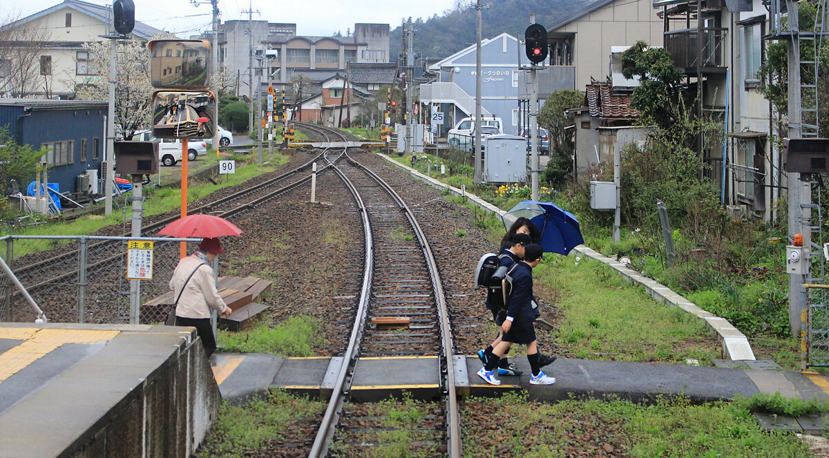 Die Chizu Kyûkô Privatbahn im Spiegel: Schüler sind aus dem Zug ausgestiegen, und der rote Schirm spiegelt sich vor Triebwagen 3504 + 3503 im Bahnsteig-Spiegel. Auf der JR Imbi Linie kurz vor Tottori, in Tsunoi, 6.April 2015. (Aufnahme aus dem frei zugänglichen hinteren Fenster) 
