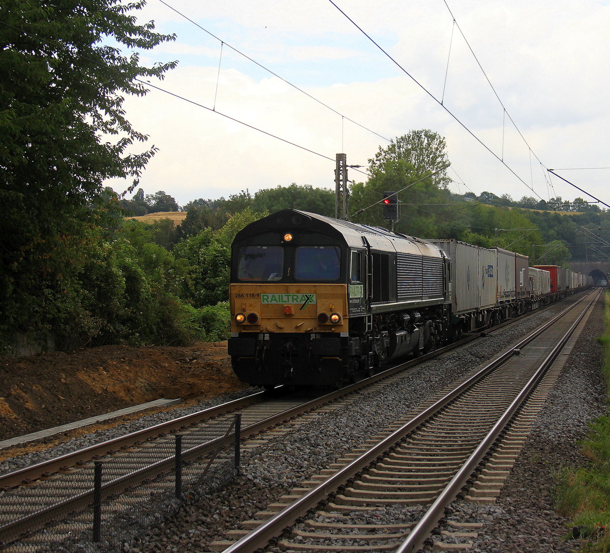 Die Class 66 266 118-9 von Railtraxx kommt mit Viel Dieselpower mit einem Containerzug aus Köln-Eifeltor(D) nach Genk-Haven(B) und kommt aus Köln-Süd,Köln-West,Köln-Ehrenfeld,Kerpen,Horrem,Buir,Merzenich,Düren,Langerwehe,Eschweiler-Hbf,Stolberg-Hbf(Rheinland) und fährt durch Aachen-Eilendorf in Richtung Aachen-Rothe-Erde,Aachen-Hbf,Aachen-Schanz,Aachen-West. Aufgenommen vom Bahnsteig 2 in Aachen-Eilendorf. Bei Sonne und Regenwolken am Nachmittag vom 12.7.2018.