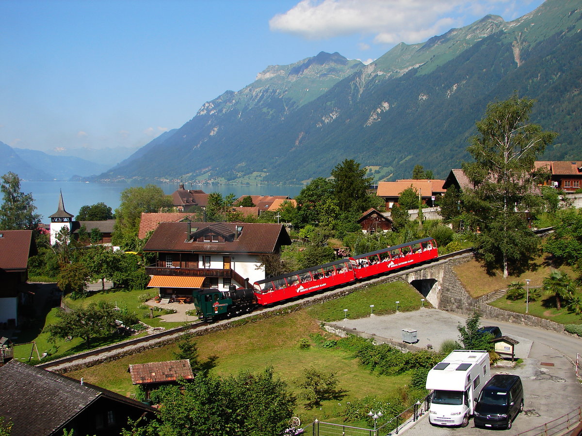 Die Dampflok 12 mit dem Zug  0836  von Brienz Rothorn Bahn verlässt Brienz auf der Rothorn Kulm. Der Abfahrt Zug  0836  ist 08 Uhr 36, und 50% billiger.
Das Bild ist von Terrasse der Unterkunft in Brienz.
05.07.2019. Brienz
