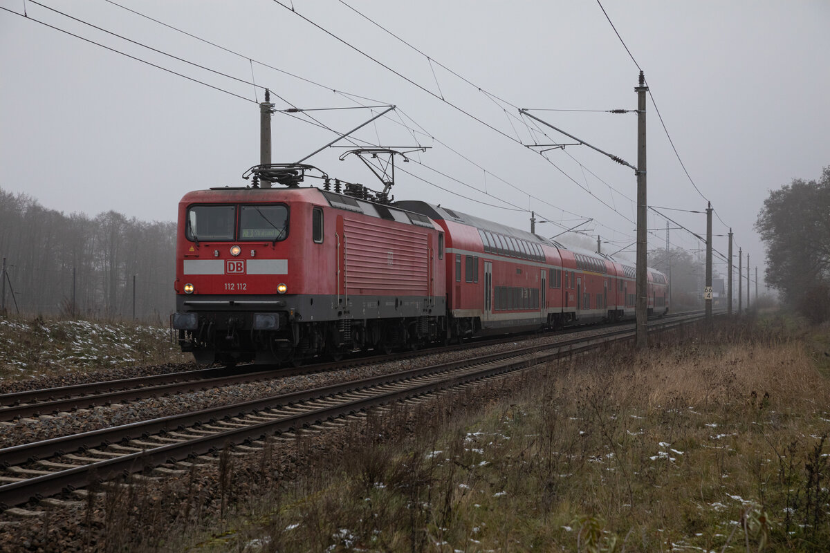 Die DB 112 112 zog am 23.11.2022 durch das neblige Herzsprung den RE3 3308 von Lutherstadt Wittenberg nach Stralsund.