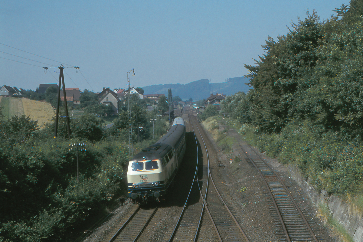 Die Diesellok 216 146 ist mit dem Eilzug Oberhausen - Walkenried auf der Sollingbahn unterwegs. Gerade hat sie den Bahnhof Volpriehausen passiert. Es ist Wochenende, die Signale des Bahnhof zeigen permanent  Fahrt frei . Die Sollingbahn war damals noch zweigleisig und hatte Güterverkehr vom Ruhrgebiet nach Nordhausen in der damaligen DDR. Dieser nimmt heute den Weg über Kassel. Das Anschlußgleis im Vordergrund gehörte einst zu einem kleinen Erzbergwerk. Volpriehausen, 19. August 1978