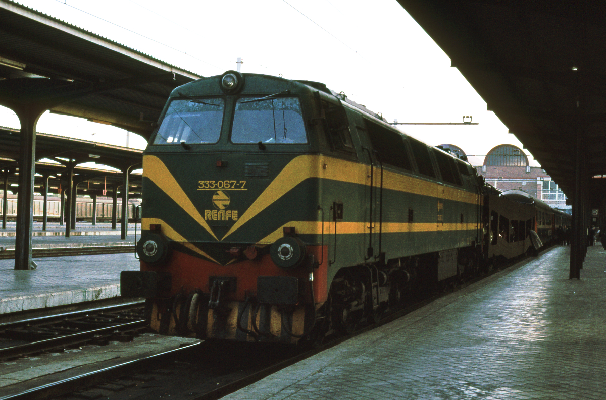 Die Diesellok 333 067 steht in Madrid Chamartin abfahrbereit mit dem Express 301  Puerta del Sol  nach Paris Austerlitz.
Er wird Madrid um 18.10 Uhr verlassen und Paris um 10.33 erreichen, oft sogar deutlich früher. 
Nur der Autotransporter und die Liegewagen der SNCF werden in Hendaye von der iberischen Breitspur auf die Normalspur wechseln und so die ganze Strecke nach Paris zurücklegen, immerhin knapp 1400 km! Im Abteil- oder Liegewagen, wo man auf dem Seitengang sich die Füße vertreten konnte, ließ sich die Strecke angenehm zurücklegen.
Oktober 1982, Canon AE1, Canoscan, GIMP