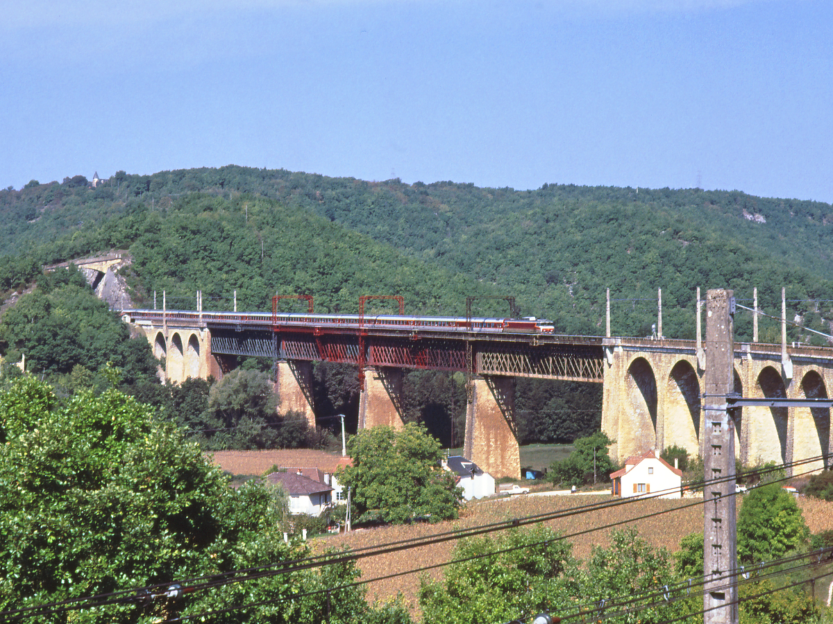 Die Eisenbahn Paris - Toulouse durchquert zwischen Brive und Montauban mit vielen Brücken und Tunnels das Massif Central. Hier führt eine CC6500 der SNCF den morgendlichen Rapide  Le Capitol  von Paris nach Toulouse. Die Aufnahme entstand im Oktober 1989 in Souillac (Dordogne). Mittlerweile wurden die Gitterbrücken durch eine moderne Konstruktion ersetzt.