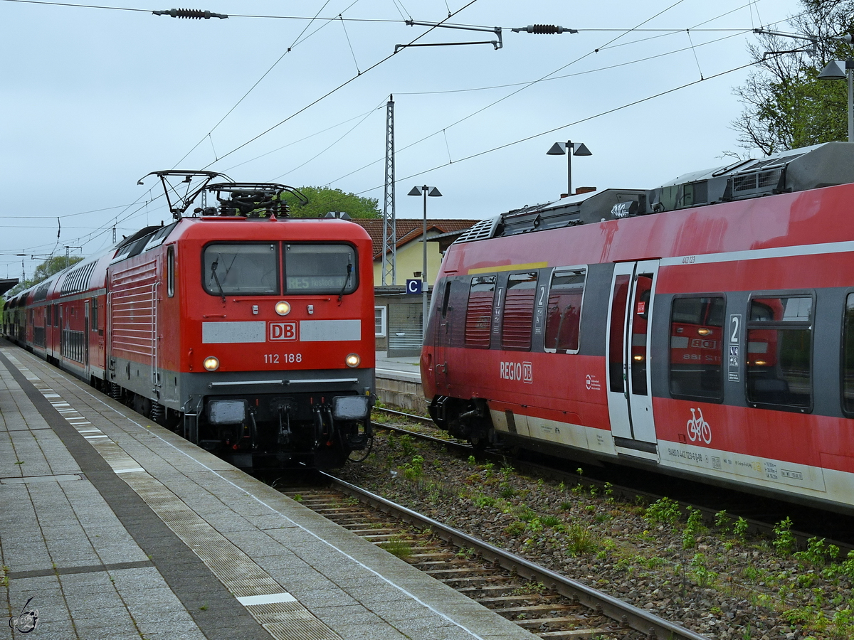 Die Elektrolokomotive 112 188 zieht eine RE-Doppelstockgarnitur in Richtung Rostock und spiegelt sich dabei im Triebzug 442 123. (Neustrelitz, Mai 2021)