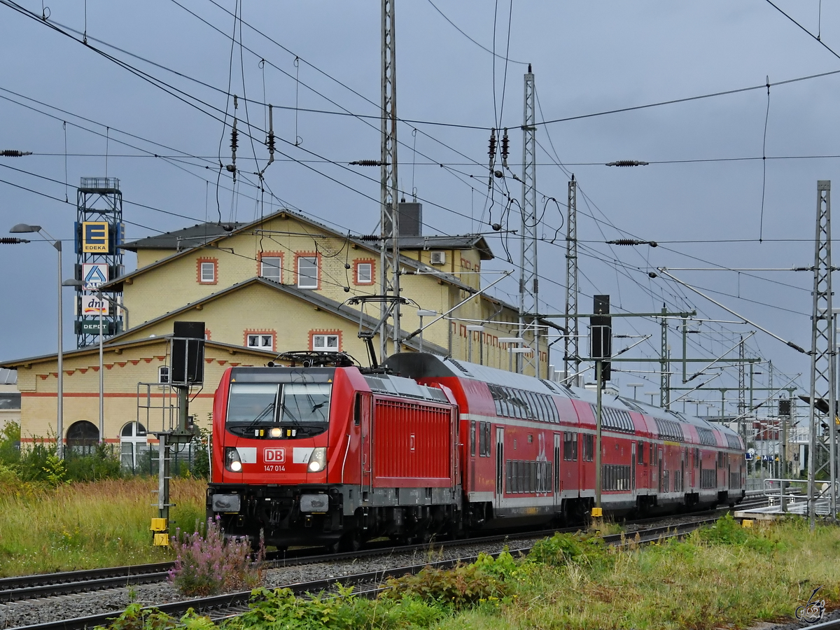 Die Elektrolokomotive 147 014 zieht als RE3 eine Doppelstockeinheit nach Stralsund, so gesehen Mitte August 2021 in der Nähe des Bahnhofes in Greifswald.