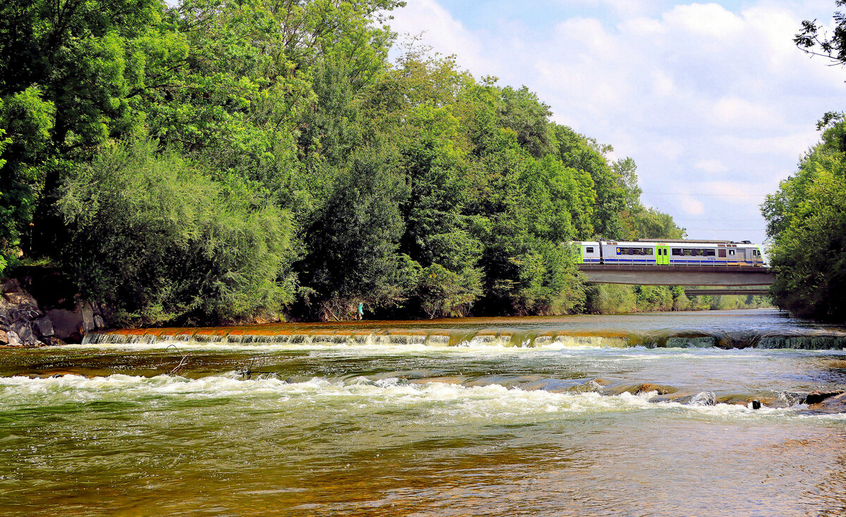 Die Emmentalbahn Burgdorf-Solothurn: Beim Emmental denkt man an die Hügellandschaft mit ihren verstreuten Bauernhöfen, doch die Emme fliesst weiter durchs Mittelland Richtung Jura, und das eigentliche Herz der Emmentalbahn ist hier der Emme entlang zwischen Burgdorf und Solothurn. Gerade überquert ein BLS NPZ Pendelzug die Emme, gestossen vom Triebwagen BLS 239, dem ehemaligen roten Triebwagen der Vereinigten Huttwil Bahnen VHB 264. Bei Aefligen, 17.August 2021 