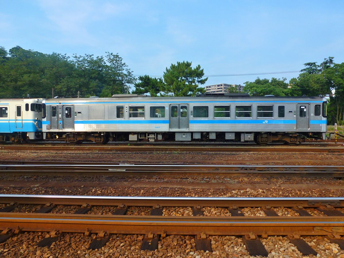 Die ersten neuen Dieseltriebwagen der damals noch jungen JR Shikoku war die Serie 1000, gebaut 1990-1998 als Nr. 1001-1056. Einmotorig, 400 PS, 21 m lang, Kasten aus rostfreiem Stahl, für Einmannbetrieb eingerichtet und häufig als Alleinfahrer unterwegs. Im Bild 1007 in Tokushima, 9.August 2013.