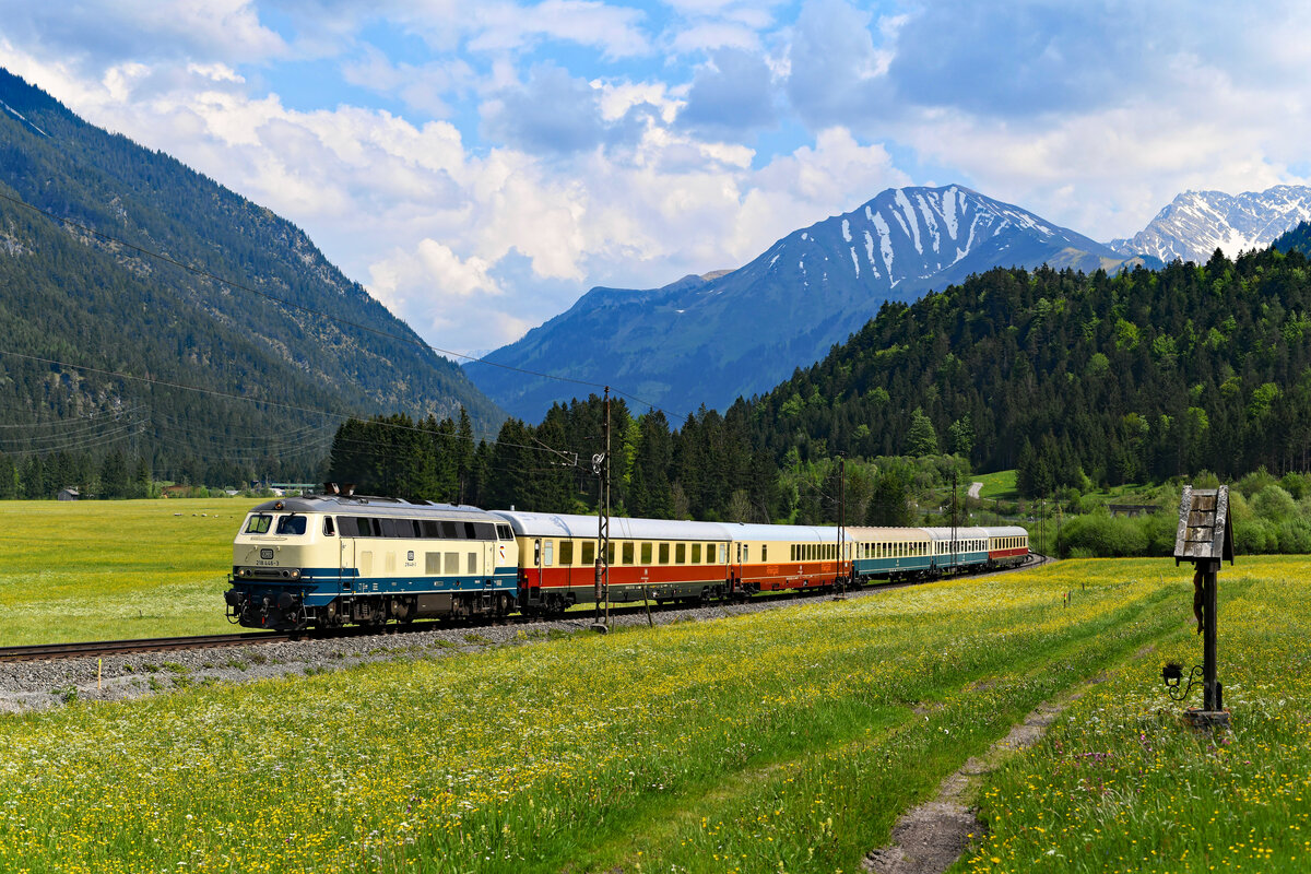 Die Fahrt des FD 523  Allgäu  durch das Außerfern fand unter wechselhaften Wetterbedingungen statt. Bei Heiterwang gelang dennoch eine Sonnenaufnahme der Sonderfahrt mit der 218 und der authentischen Wagengarnitur. Blühende Wiesen, ein Marterl und der Blick auf das 1.906 Meter hohe Gartner Joch boten den perfekten Rahmen für ein Bild der Fahrt über diese wunderschöne Gebirgsbahn. Man beachte auch die an dieser Stelle noch vorhandenen alten Fahrleitungsmasten, die noch aus der Anfangszeit der Bahn stammen. Darüber hinaus bekommt man auch einen Eindruck der ordentlichen Steigungen, die es hier zu bewältigen gilt. Die 218 hat das aber alles mit Bravour gemeistert.   