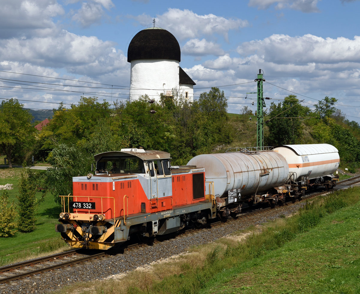 Die von FAUR S.A. in Bukarest gefertigte MAV M47 478 332 brachte am 19.09.2019 zwei Kesselwagen aus der Düngemittelfabrik Péti Nitrogénművek Zrt. Petfürdö nach Veszprém,
und wurde von mir in Öskü  vor der Kulisse der Ende des 11. Jahrhunderts errichteten Rundkirche  Ösküi kerektemplom  fotografiert.
