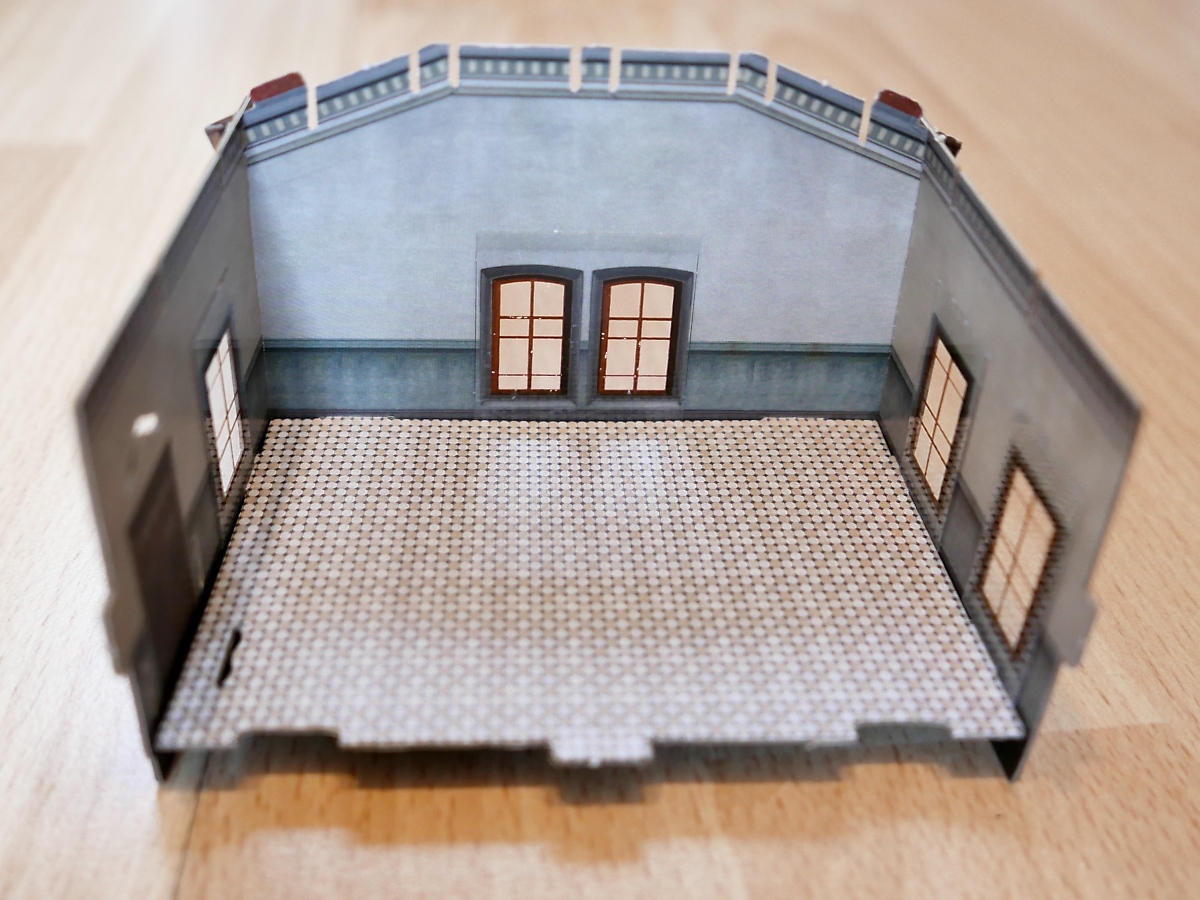 Die Fenster-Einsätze sind als einziges nicht aus Karton. Bedruckter Klarsicht-Kunststoff wird von innen auf die Ausschnitte geklebt. Dank schon aufgetragenen Klebestreifen ist kein Hantieren mit Klebstoff nötig.

Hier sieht man, dass die Innen- bzw. Rückseiten der Bauteile ebenso fein wie die Außenseiten detailliert sind.

Zuhause, 21.12.18