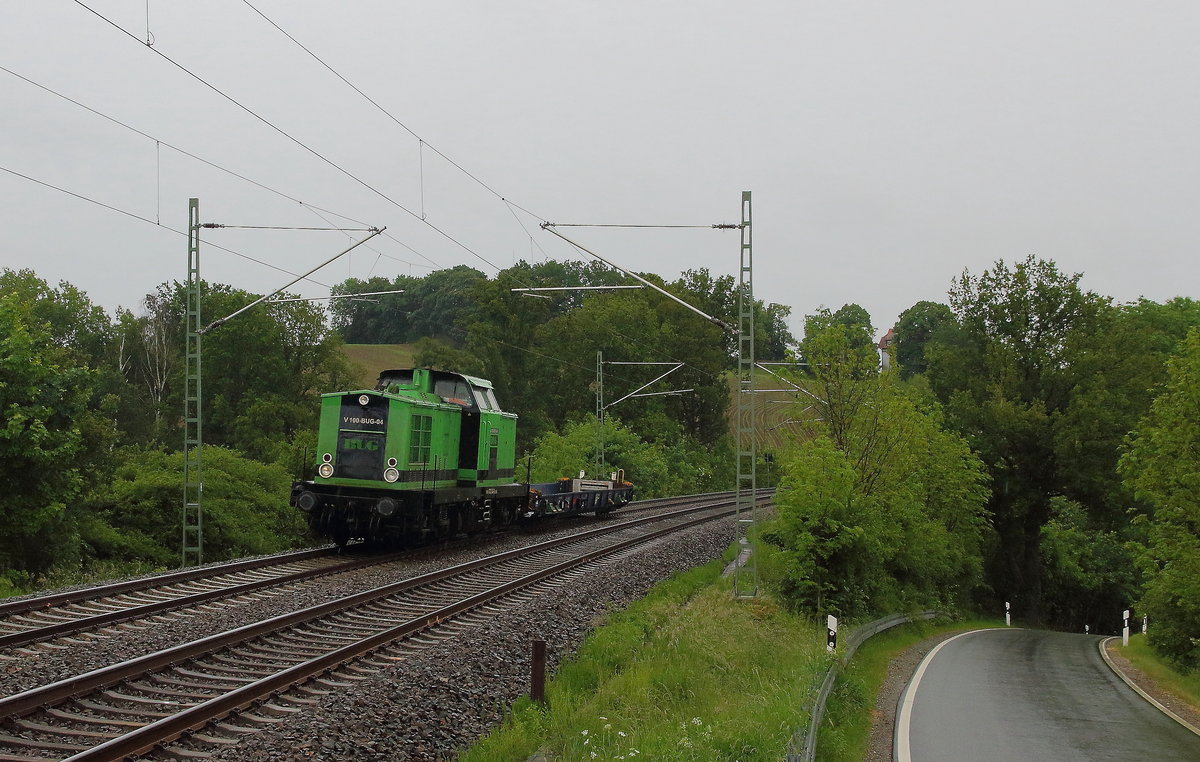 Die grün schwarze V100 der BUG Verkehrsbau AG mit einen Rola-Wagen bei Jocketa/ Pöhl bei beginnenden Regenwetter am 07.06.2020