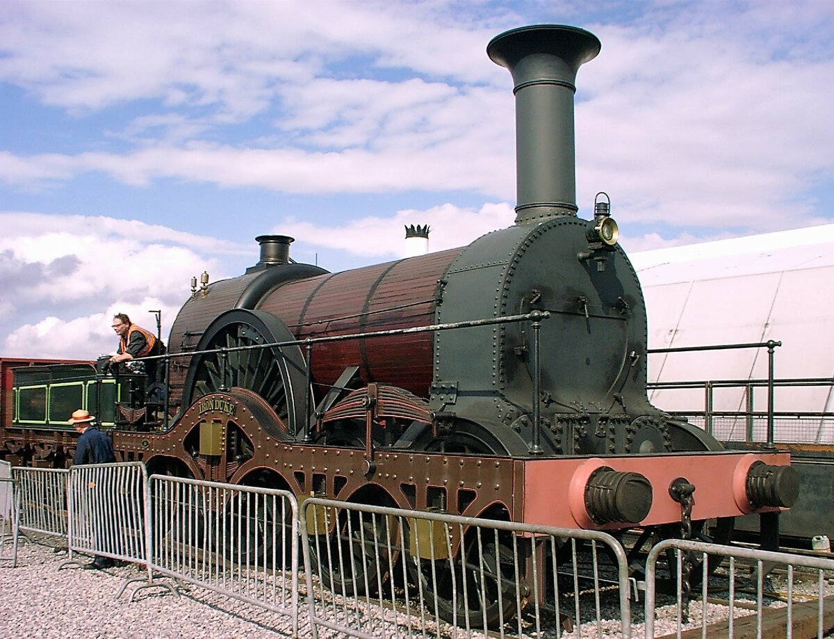 Die GWR Class Iron Duke war eine Baureihe von Breitspur–Dampflokomotiven für Schnellzüge der Great Western Railway. Achsformel 2A1, Spurweite 2140 mm, Treibraddurchmesser 2,44 m und Höchstgeschwindigkeit 128km/h, die Treibachse war spurkranzlos. Die Ausmusterung erfolgte bereits 1892. Hier handelt es sich um eine 1985 gebaute betriebsfähige Replik im Originalmaßstab, die ich unter Dampf am 27.8.2000 auf dem Freigelände des National Railway Museum in York auf einer Parallelfahrt mit der Rocket erleben durfte. Für Modelleisenbahner: das ist wie wenn eine H0-Lok neben einer TT-Lok fährt 😂
In den 1860er Jahren sah die GWR ein, daß sie den Spurweitenkrieg nicht gewinnen konnte und die Breitspur sich nicht durchsetzen würde. Schritt für Schritt baute die GWR das Breitspurnetz auf Normalspur um, wobei teilweise als Zwischenlösung Dreischienengleise verlegt wurden. Die Fusion mit der West Midland Railway führte dazu, daß der Bahnhof Paddington 1861 erstmals von normalspurigen Zügen bedient wurde. Nach 1869 gab es nördlich von Oxford keine Breitspurgleise mehr. Der Umbau des letzten Breitspurabschnitts erfolgte im Mai 1892.