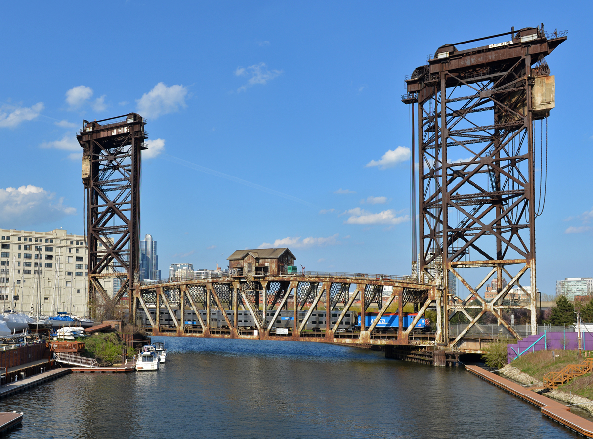 Die imposante 56,4 Meter hohe Canal Street Railroad Bridge bzw. Pennsylvania Railroad Bridge wie die fotogene Stahlfachwerk-Hubbrücke auch genannt wird wurde am 30. Juli 1914 fertiggestellt und führt über den Chicago River. Am 24. April 2016 fotografierte ich den Metra Zug 917 Heritage Corridor (HC)von Chicago Union Station nach Joliet bei deren Überquerung, gezogen von  F40PH 105.