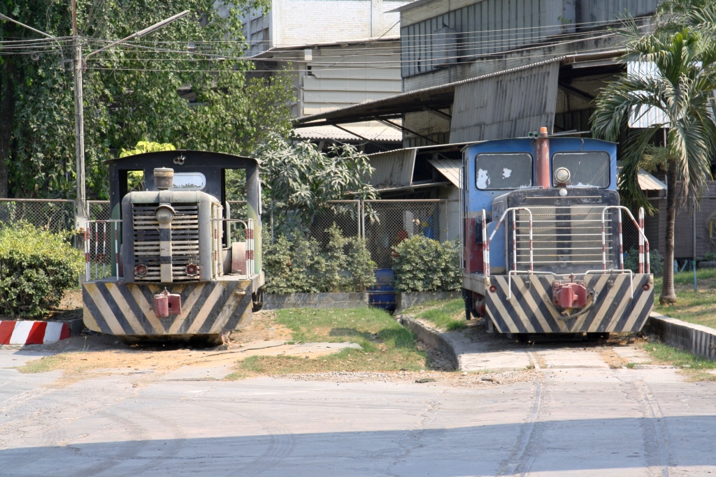 Die Jalaprathan Cement Factory bei der Phon Thong Station war einst an die Northern Line angeschlossen. - Zur Bedienung dieser, nunmehr größtenteils abgetragenen Anschlussbahn standen 2 werkseigene Diesellokomotiven zur Verfügung welche nun beim Werkseingang auf einem Gleisrest aufgestellt sind. - Leider konnte ich keine Informationen über Type und Hersteller dieser Loks bekommen. - Die blau lackierte Lok trägt zwar das Firmenlogo von Horikawa Kohki (Japan), allerdings um 180° verdreht montiert. - Bild vom 29.März 2023.