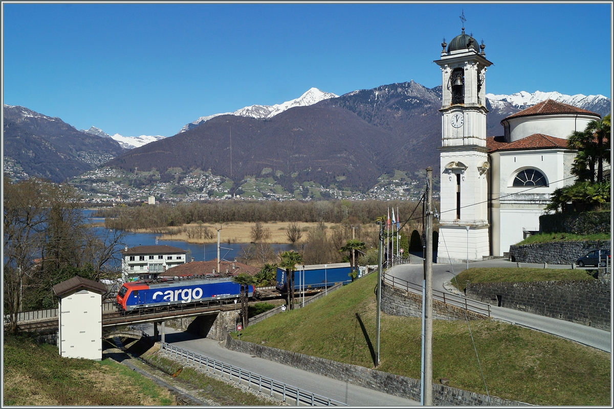 Die Kirchuhr der schönen Kirche San Carlo von Magadino zeigt kurz vor eins, als eine SBB Re 474 mit ihrem Güterzug durch den ruhigen Feiertag (San Giuseppe) Richtung Luino fährt. 19. März 2014