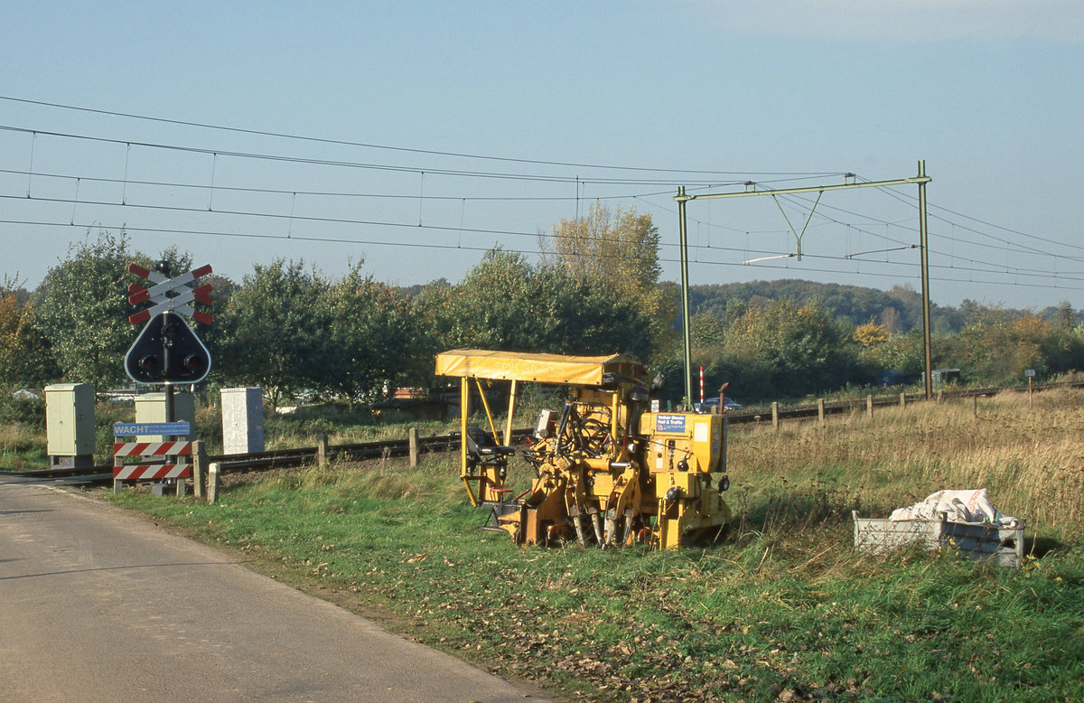 Die kleine Stopfmaschine der Fa Volker Stevin, nach nächtlicher Arbeiten abgestellt neben dem Gleis zwecks abholung durch den LKW.
Babberich, Kwartiersedijk, am 23.10.2000.
Fab: Plasser & Theurer, F.Nr.2794, Bjr.1992, Typ PKS.
Diascan (Fujichrome).
Dieser Bahnübergang wurde später entfernt. Heute stehen hier hohe Schallschutzwände.