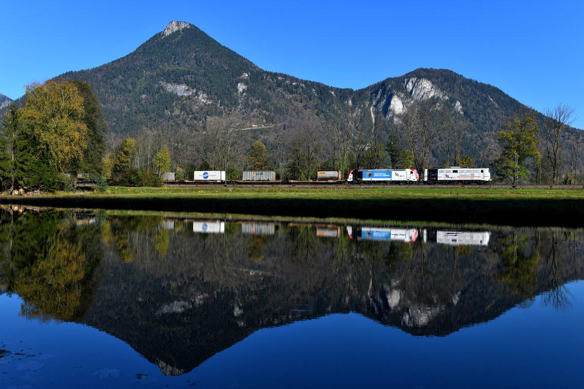 Die Kombiverkehr KG feierte 2019 ihr 50-jähriges Firmenjubiläum. Um auf dieses Ereignis hinzuweisen wurde die 139 135 von Lokomomotion mit einem eigenständigen Design versehen. Statt der blauen Zebrastriefen zieren die Einheits-E-Lok nun ein orange-roter Streifen und eine entsprechende Beschriftung. An einigen Tagen wurde sie im Tandem mit der 185 665 vor einem KLV-Zug in Verkehr gesetzt und die Fahrten vorab für interessierte Fotografen in sozialen Netzwerken publiziert. Der letzte dieser Einsätze fand am 26. Oktober 2019 statt, als die fotogene Doppeltraktion vor dem DGS 43119 von München Ost Rbf bis zum Brenner zum Einsatz kam. Zwischen Kirnstein und Niederaudorf wurde das stillstehende Gewässer genutzt, um eine Spiegelung des Zuges samt Kranzhorn im Hintergrund umzusetzen. Ein Angelegenheit, bei der es um Sekunden ging, wie es der Schatten erahnen lässt. Einen Augenblick später lag das Motiv bereits im Dunklen. 