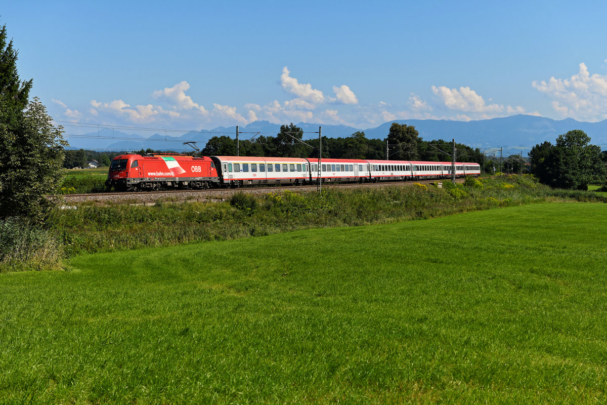 Die letzte ihrer Art war zum Aufnahmezeitpunkt die 1216.015 - trug sie doch noch die italienische Flagge auf ihren Seitenwänden. Damit wurde einst bei mehreren Loks der Baureihe auf die Übernahme des Schnellzugverkehrs über den Brenner durch die ÖBB und die DB hingewiesen, nachdem die FS daran kein Interesse mehr zeigte. Inzwischen haben fast alle Maschinen diese äußere Gestaltung verloren, da sie im Rahmen einer Hauptuntersuchung Neulack erhielten. Am 07. August 2020 brachte die besagte 1216.015 den EC 80 von Verona Porta Nuova nach München HBF und konnte von mir bei Rann im bayerischen Voralpenland aufgenommen werden. 