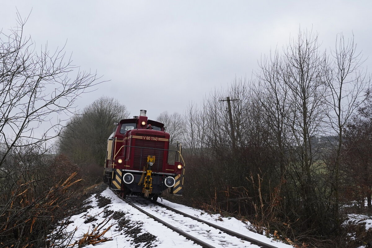 Die Lok V60 1140(98 80 3365 140-3 D-VEB) der Vulkan-Eifel-Bahn(VEB) führt die Überführungsfahrt auf der Eifelquerbahnstrecke an. Die Lok wurde 1963 bei der MaK in Kiel unter der FNr.600455 gebaut und bei der DB-V60 1140 in Dienst gestellt, wo sie ab 1968 dann die EDV-Nummer 261 140 erhielt.
Die zweite Überführungsfahrt von Gerolstein über die dafür wieder befahrbar gemachte Eifelquerbahn nach Kaisersesch und dann weiter nach Andernach fand am 18.01.22 statt.
Die Fahrzeuge waren seit der Hochwasserkatastrophe die die Eifelbahn unbefahrbar machte, im ebenfalls davon betroffenen Bahnhof Gerolstein eingeschlossen gewesen.

2022-01-18 Darscheid Feldweg-BÜ