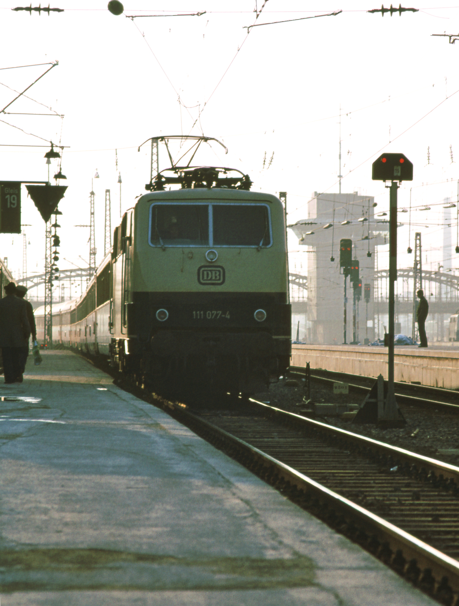 Die Lokomotive 111 077 der Deutschen Bundesbahn fährt mit dem D265 Strasbourg - Wien kurz nach 17 Uhr in den Münchner Hauptbahnhof ein. Die 111 hat ihren Zug in Stuttgart übernommen. Er besteht aus Eurofima-Waggons der ÖBB und Corail der SNCF. Der Fahrplan von 1983 weist den Zug als FD265  Mozart  Paris - Wien aus, mit Abfahrt in Paris Est um 7.45 und Ankunft in München um 17.01. München Hauptbahnhof, 22. März 1980