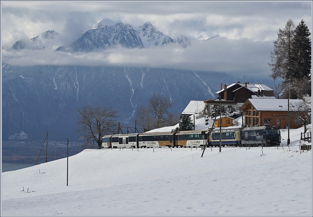 Die MOB Ge 4/4 8003 zieht kurz vor Les Avants den recht bunten IR 2122  MOB Panoramic  Richtung Zweisimmen. Links im Bild ist der Genfersee zu erkennen und damit der Höhenunterschied, welcher der Zug seit seiner Abfahrt vor gut einer halben Stunde in Montreux bewältigt hat.
3. Feb. 2018