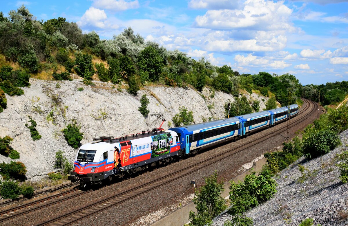 Die neueste Werbelok von MÁV Start is die 470 002. Die Lokomotive trägt Werbung für die 75 Jahre Alt Kindereisenbahn (Budapest - Széchenyi-hegy).
An ihrem zweiten Arbeitstag in neuen Outfit ist mit dem Zug IC926  Savaria  aus Budapest-Keleti nach Szombathely kurz vor die Hst. Szár.  
29.07.2023.