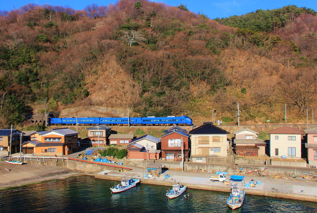 Die Nordwestküste Japans, Hauptlinie Niigata - Akita am Japanischen Meer: Zweistrom-Expresszug Serie 653 Nr.1006 im Fischerdörfchen Wakigawa. 18.März 2019 