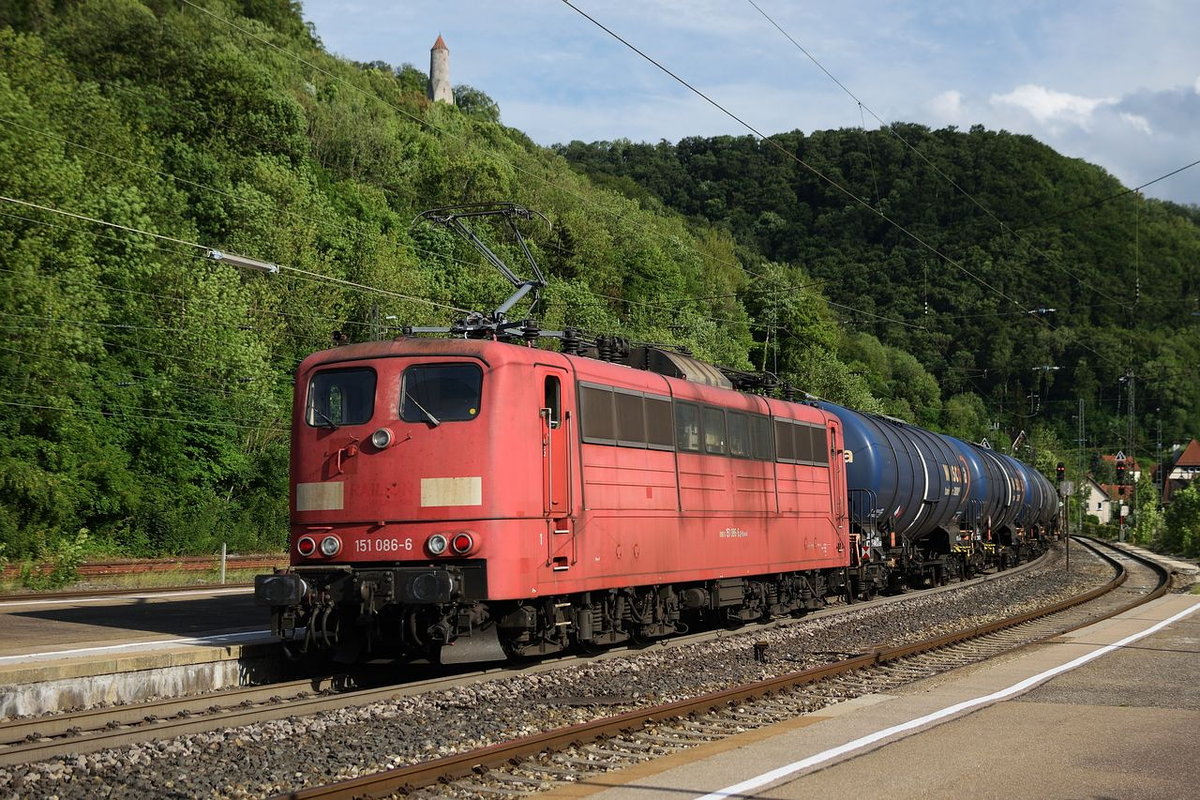 Die orientrote 151 086 hat am 21. Juni 2018 Schiebedienst an der Geislinger Steige. Hier hilft sie einem langen Kesselwagenganzzug durch den Bahnhof von Geislingen, an welchen sich unmittelbar die gleichnamige Steige anschließt.