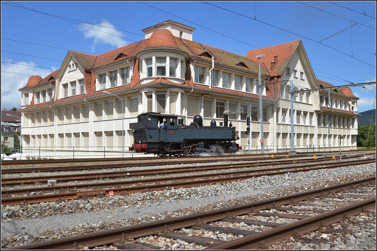 Die portugiesische Dampflok G 2x2/2 E 164 unter der Flagge von La Traction im August 2016 in Tavannes vor dem eindrucksvollen Gebäude der Tavannes Watch CO.