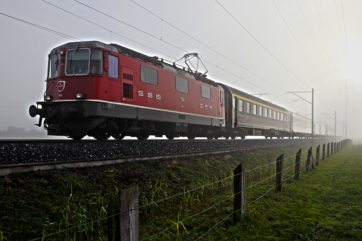 Die Re 4/4 II 11154 taucht aus dichtem Nebel kommend mit dem EN Belgrad-Zürich HB auf.Bild in Bilten 14.11.2014