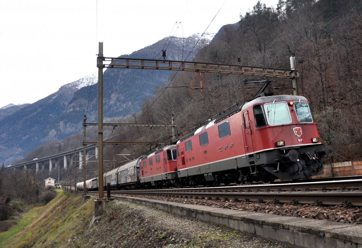 Die Re 4/4 III 11370 und die Re 4/4 II 11245 fahren mit ihrem kurzen Güterzug nordwärts, links ist das Gebäude der ehemaligen Station Giornico zu erkennen, aufgenommen am 19.12.2014. 