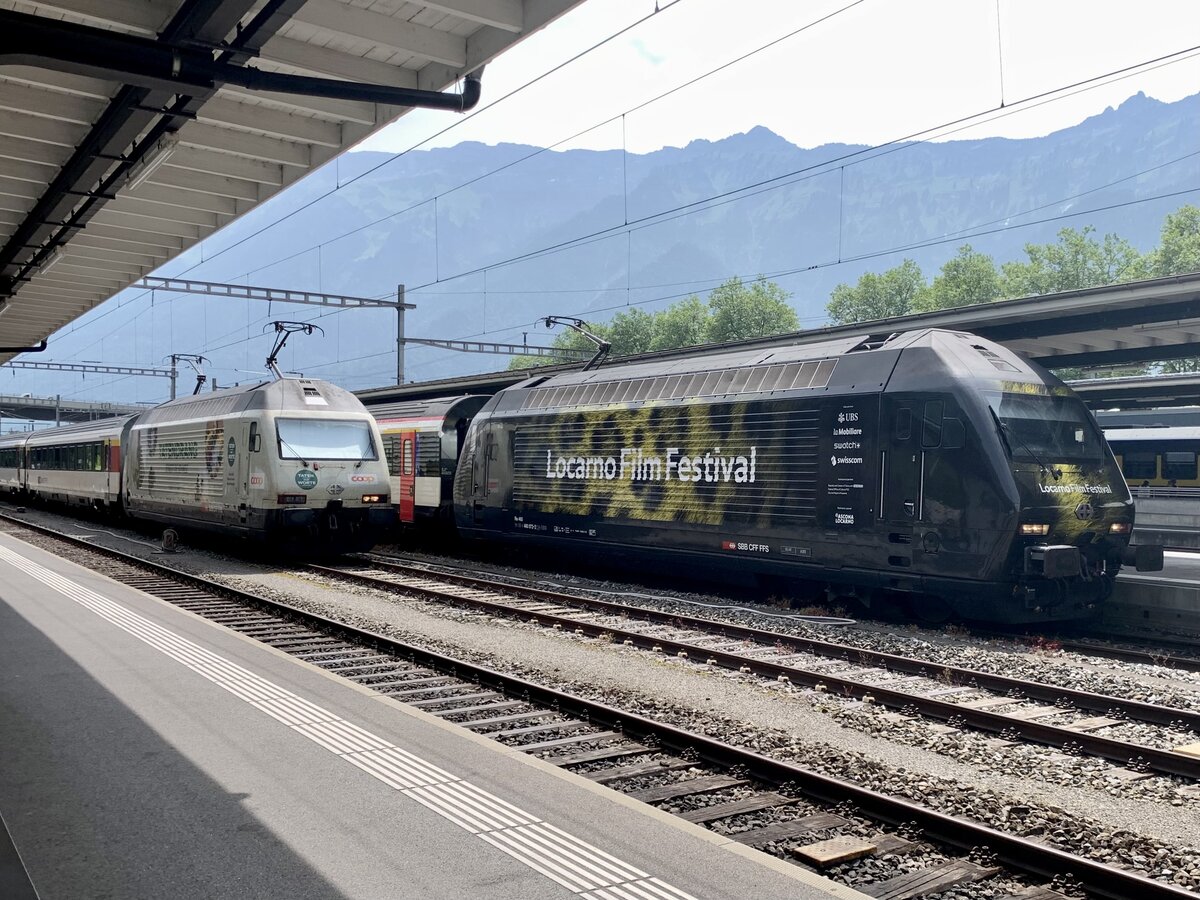 Die Re 460 041  Coop Tatendrang  an einem Zusatzmodul abgestellt mit der Re 460 072  Locarno Film Festival  die am EC nach Hamburg-Altona bereit steht, am 21.6.23 im Bahnhof Interlaken Ost.