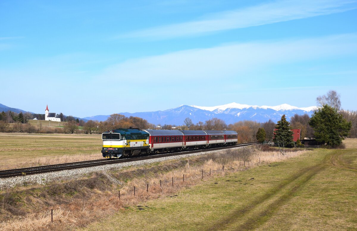 Die retrolackierte  Taucherbrille  754 055  Renátka  ist auf dem Weg von Vrútky (Rutteck) nach Zvolen (Atlsohl) mit dem R937  FATRAN  bei Blažovce. Im Hintergrund sind die Kirche von Turčiansky Ďur und die schneebedeckte Fátra zu sehen. 18.03.2023.