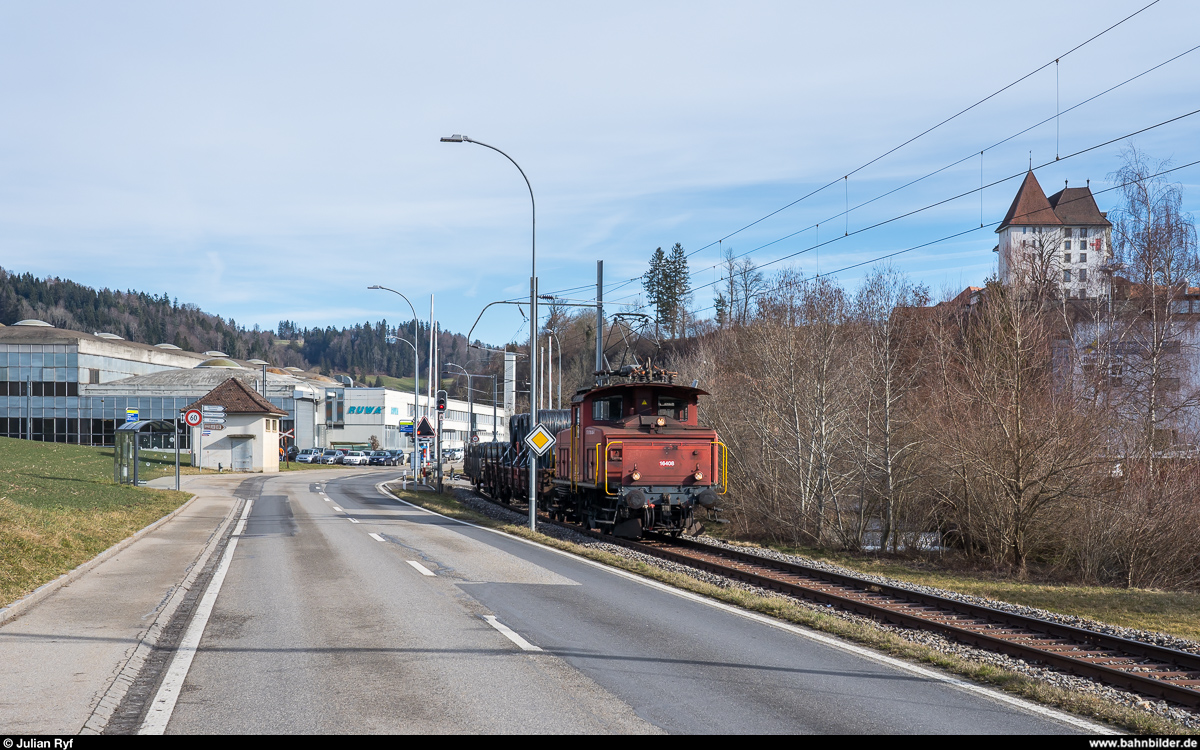 Die RUWA Drahtschweisswerk AG in Sumiswald besitzt zwei Ee 3/3, welche sie für die Überfuhr der von SBB Cargo in Sumiswald-Grünen angelieferten Güterwagen zu ihrem Werk im Ortsteil Burghof an der nicht mehr für den Personenverkehr genutzten Strecke Richtung Wasen nutzt. Da die Entladerampe im firmeneigenen Anschlussgleis nur Platz für zwei Wagen bietet, werden die Wagen im Bahnhof Sumiswald-Grünen gelagert und von der Ee 3/3 jeweils paarweise ins Werk zum Entlad und danach gleich wieder zurück gebracht. Ich habe den morgendlichen Wagenwechsel am 20. Februar 2020 fotografisch dokumentiert.<br>
Eine knappe halbe Stunde nachdem die leeren Wagen in den Bahnhof gebracht wurden, kehrte die Ee 3/3 16408 mit zwei vollen Wagen wieder zurück. Vor der Einfahrt ins Werk muss dabei zuerst die mit einem modernen Bahnübergang gesicherte Steinweidstrasse und danach, bereits nach der Weiche ins Anschlussgleis, die ungesicherte Eystrasse gequert werden. Die Ansteuerung des Bahnübergangs erfolgt manuell durch den Rangierer, weshalb davor ein Halt nötig ist. Rechts oben das Schluss Sumiswald.