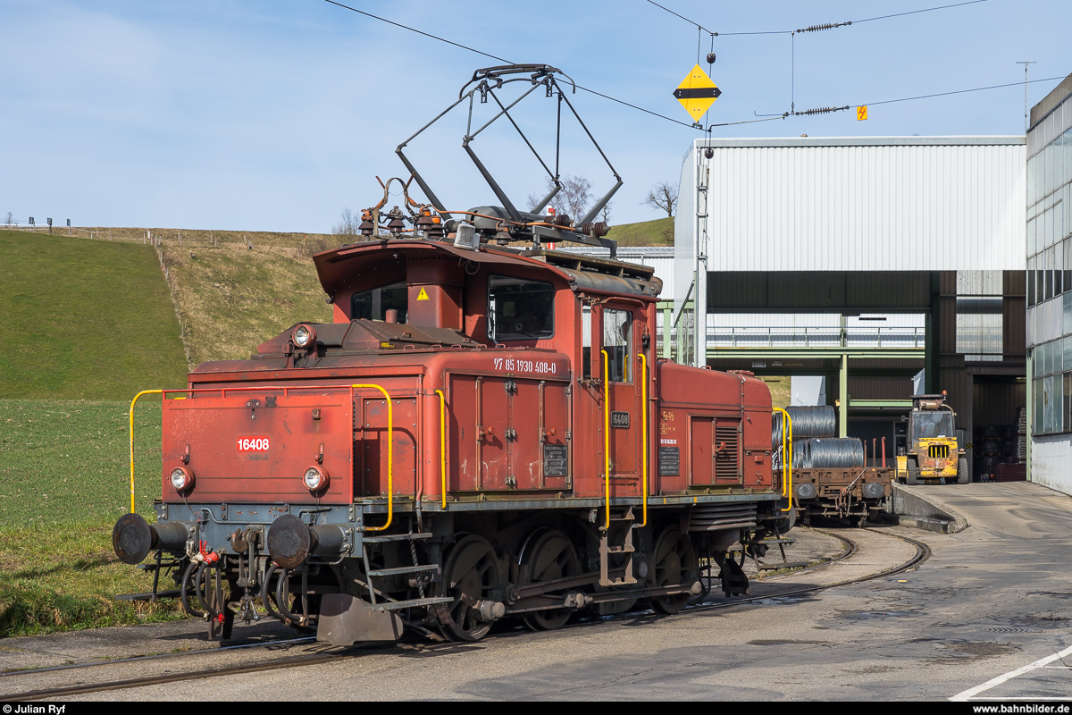 Die RUWA Drahtschweisswerk AG in Sumiswald besitzt zwei Ee 3/3, welche sie für die Überfuhr der von SBB Cargo in Sumiswald-Grünen angelieferten Güterwagen zu ihrem Werk im Ortsteil Burghof an der nicht mehr für den Personenverkehr genutzten Strecke Richtung Wasen nutzt. Da die Entladerampe im firmeneigenen Anschlussgleis nur Platz für zwei Wagen bietet, werden die Wagen im Bahnhof Sumiswald-Grünen gelagert und von der Ee 3/3 jeweils paarweise ins Werk zum Entlad und danach gleich wieder zurück gebracht. Ich habe den morgendlichen Wagenwechsel am 20. Februar 2020 fotografisch dokumentiert.<br>
Während die gerade ins Werk gebrachten Wagen mit einem Gabelstapler an die Rampe befördert und danach entladen werden, bleibt die Ee 3/3 16408 am Ende der Fahrleitung am Rand des Werkgeländes stehen.