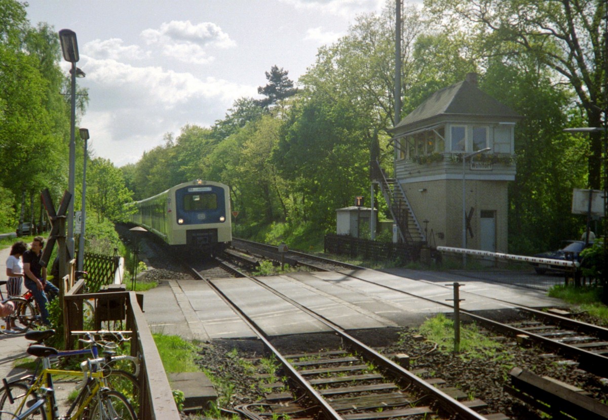 Die S-Bahn-Haltepunkt mit Blockstelle Wohltorf im Sachsenwald am 17.05.1992 mit einfahrender S 21 (Hamburg Elbgaustrae–Aumhle); heute liegen hier vier von Lrmschutzwnden umgebene Gleise (2 x S-Bahn, 2 x Fernbahn), und der Bahnbergang  Eichenallee  ist einer Straenunterfhrung gewichen.