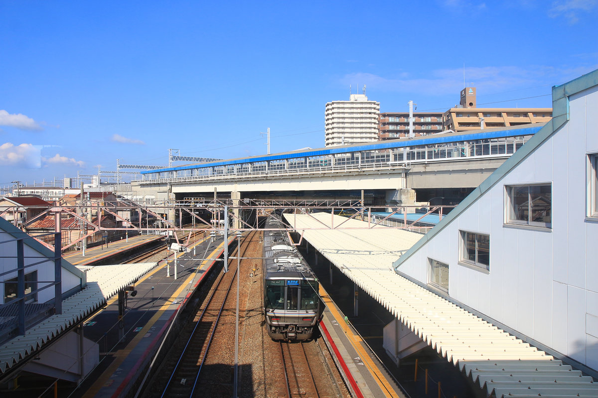 Die S-Bahn im Kansai-Gebiet, Sanyô Hauptlinie der Inlandsee entlang westlich von Ôsaka. Endlich kommt hier in Nishi Akashi auch die vierte Doppelspur durch dieses Gebiet zum Vorschein, nämlich der Hochgeschwindigkeitszug Sanyô Shinkansen. Dieser hat die circa 60 km von Ôsaka bis hierher praktisch durchgehend im Tunnel (mit sehr abwechslungsreicher Aussicht auf eine schwarze Tunnelwand) zurückgelegt. Im Bild steht ein S-Bahnzug Serie 223 (Endwagen KUMOHA 223-2054 aus dem Jahr 2003) unter dem Shinkansen-Bahnhof Nishi Akashi. 6.November 2018   