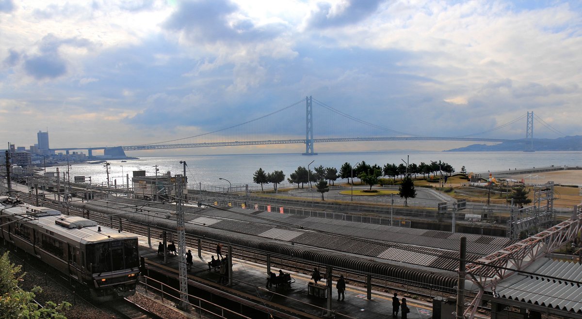 Die S-Bahnlinie von Ôsaka über Kôbe der Inlandsee entlang nach Westen kommt an der weltgrössten Hängebrücke (3911 m) über die Akashi-Meeresenge vorbei. Diese Brücke bildet den Uebergang von der japanischen Hauptinsel auf die Insel Awaji in der Bucht von Ôsaka, von der aus dann eine weitere riesige Brücke auf die Insel Shikoku hinüber führt. Diese direkte Strassenverbindung nach Shikoku wurde 1998 eröffnet. Von den 3 grossen Brückenverbindungen auf die Insel Shikoku hat jedoch nur die mittlere (vom Raum Okayama aus) auch eine Bahnlinie (1988 eröffnet). Im Bild fährt ein  Neuer Eilzug  der Serie 223, der nur an ganz wenigen Stationen hält, auf der obersten der 3 Doppelspuren ohne Halt am Bahnhof Asagiri vorbei. Die unteren beiden Doppelspuren sind für die JR-Züge mit Halt an allen Stationen, und für die Züge des Grosskonzerns Elektrische Sanyô Bahn (Sanyô Dentetsu). 6.November 2018   SANYÔ HAUPTLINIE 
