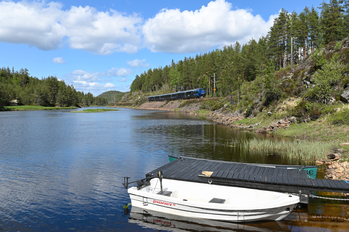 Die Sørlandsbanen überquert auf ihrer Fahrt von Oslo nach Stavanger zahlreiche Flüssen und Seen. Rund 40 km nördlich von Kristiansand folgt die Bahn für einige Kilometer dem Fluss Rettåna, welcher mehrere Seen miteinander verbindet. Am 26.05.2022 ist Reg 711 zwischen Herefoss und Vennesla in Richtung Kristiansand unterwegs.