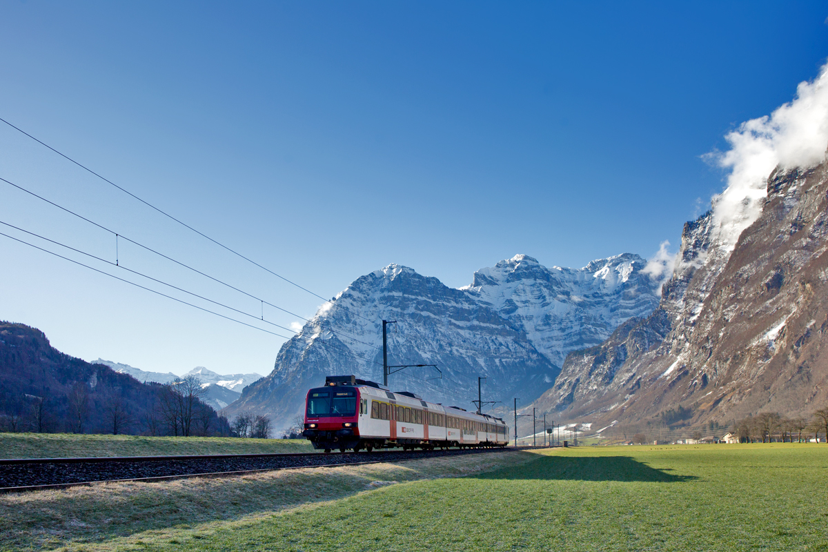Die S6 nach Rapperswil fährt am Vormittag,wenige Sekunden nach Sonnenaufgang im Tal, am 11.2.2016 in Mollis vorüber.
