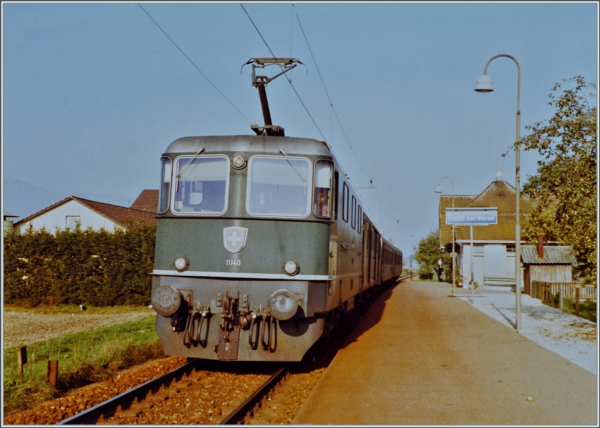 Die SBB Re 4/4 II 11140  beim Halt in Rüti bei Büren mit ihrem Regionalzug von Herzogenbuchsee nach Lyss. 
Die Strecke von (damals) Neu Solothurn nach Busswil wurde am 4. Dezember 1876 eröffnet und am 3. Oktober 1944 elektrifiziert. 1994 wurde der Personenverkehr auf dem Abschnitt Solothurn - Büren an der Aare eingestellt, für das Tanklager  Thomen  verkehren jedoch auch weiterhin Zustellfahren, die Zeitweilig verkehrenden Dampfzüge von Solothurn nach Büren a/A mussten 2016 infolge einer maroden Brücke bei Büren eingestellt werden.  

Ein Analogbild vom Oktober 1984