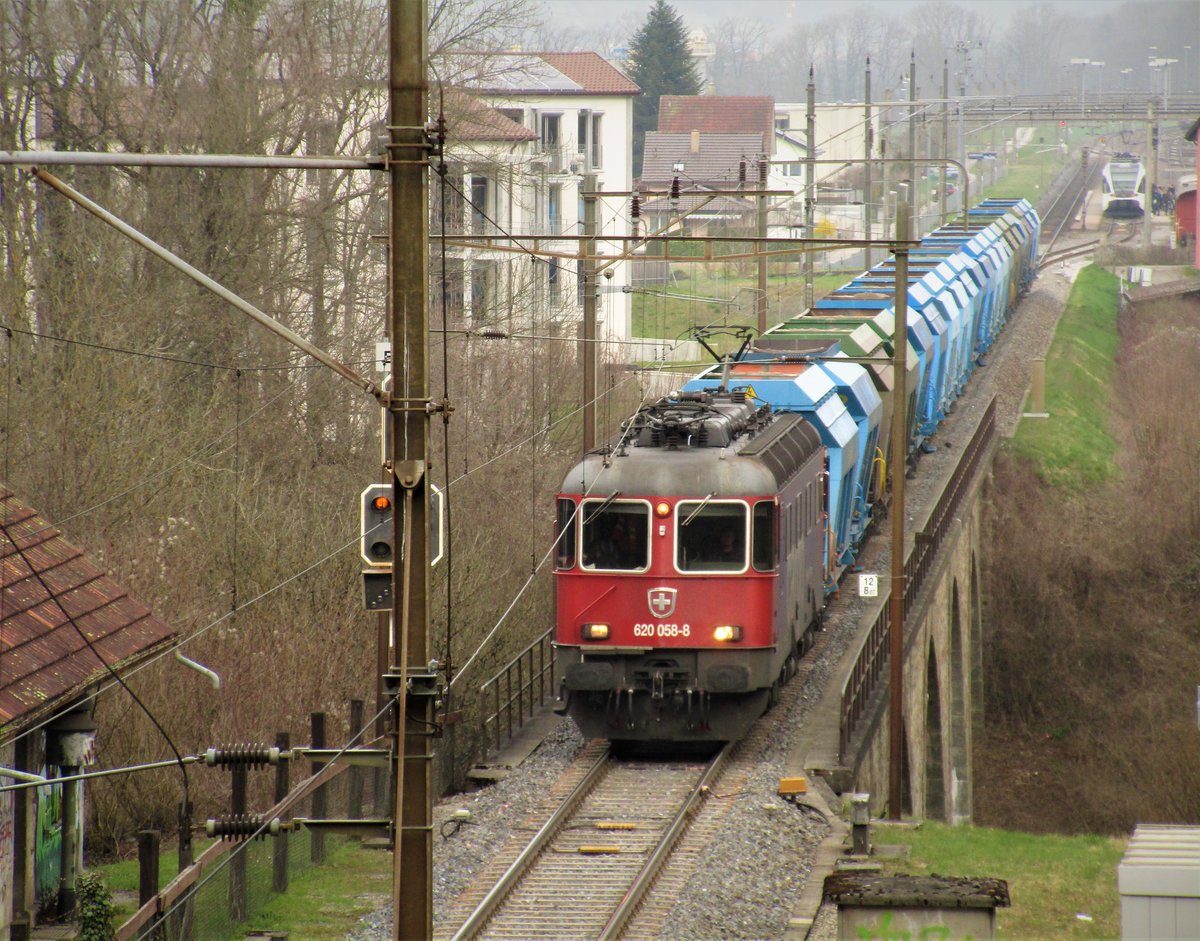 Die SBB Re 620 058-8 | SBB Re 6/6 11658  Auvernier  durchfährt im Bild am 24.3.17 mit einem Kieszug mit vielen leeren HASTAG AG Waggons die 93 Meter lange Wildbachbrücke bei Embrach, welche 1950 durch einen Neubau ersetzt wurde. Der Kieszug fuhr von Winterthur zum Bahnhof Embrach-Rorbas, wo der Kieszug eine kurze Zeit lang auf eine S41 wartete, um eine freie Durchfahrt nach Bülach gelangen. Währendem im Hintergund die Thurbo RABe 526 790-1 als S41 auf seine Abfahrt nach Winterthur wartet und Fahrgäste hineinsteigen, hat der langer Kieszug freie Durchfahrt in den 1,8 km langen einspurigen Dettenberg-Tunnel, der nach Bülach führt. Auf dieser Strecke verkehrt hauptsächlich nur die S41 Winterthur-Bülach(-Waldshut)), und sonst wenige Güterzüge, wie auch Dienstzüge. Die Aufnahme entstand genau auf dem Ostportal des Dättenberg-/Dettenbergstunnels.