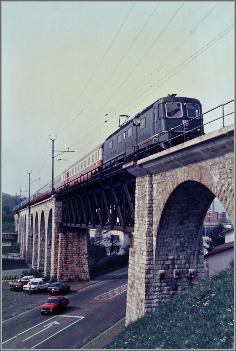 Die SBB Re 6/6 11645  Colombier  ist mit dem IC 375  Mont-Blanc  von Genève nach Hamburg auf dem Weg nach Delémont und überquert unmittelbar vor dem Bahnhof Grenchen Nord den BLS / MLB Mösli Viadukt. 

Analogbild vom April 1985