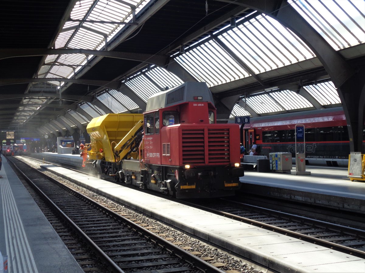 Die SBB Tm 234 000-8  Ameise  hatte am Morgen des 16. Juli 2018 im Hauptbahnhof Zürich einen Kieswagen im Schlepp. Dabei leert der Schotterwagen neue Schottersteine über dem Gleis 9, währenddem die  Ameise  in sehr tiefer Geschwindigkeit aus der Bahnhofshalle fährt.